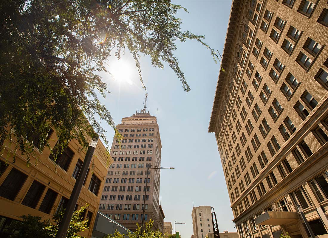 Business Insurance - View Looking Up at Commercial Buildings Next to Green Trees in Downtown Fresno California Against a Sunny Blue Sky